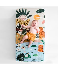 a baby laying on top of a blanket next to a wallpaper covered in jungle animals