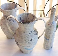 three vases made out of newspaper sit on a table with chairs in the background