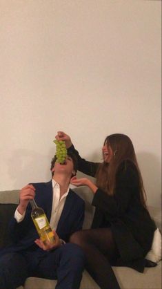 two people are sitting on a couch and one is holding a bottle of wine while the other holds a green object