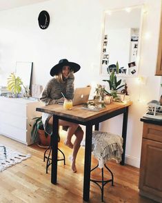 a woman sitting at a table with a laptop computer on her lap and wearing a cowboy hat