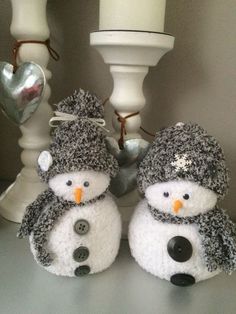 two snowmen with hats and scarves are sitting next to a white candle holder