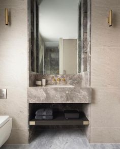 a bathroom with marble walls and flooring next to a white sink under a large mirror