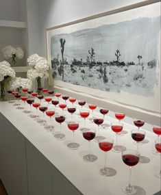 many wine glasses are lined up on a long table with white flowers in vases