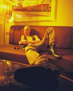 a man sitting on top of a brown couch next to a table with a glass coffee table