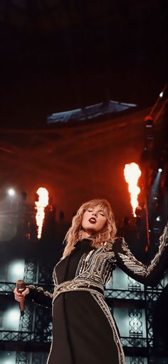 a woman standing on top of a stage wearing a black dress and holding a microphone