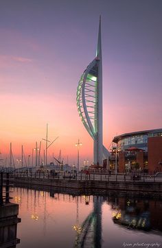 a very tall building sitting next to a body of water at sunset with boats in the background