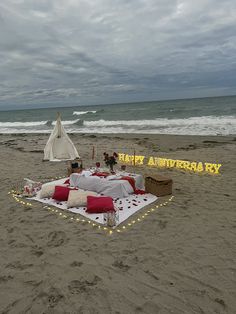 a blanket and pillows on the beach with an umbrella in the sand next to it