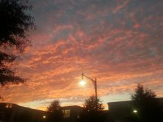 the sun is setting over some buildings and street lights with clouds in the sky above