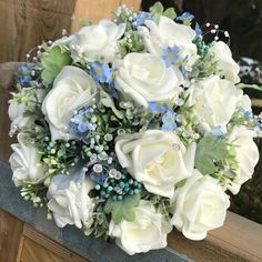 a bridal bouquet with white roses and blue flowers on a wooden bench outside in the snow