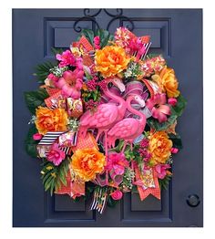 a pink flamingo wreath is hanging on a blue door with flowers and ribbon around it