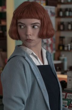 a woman with red hair standing in front of a store counter and looking at the camera