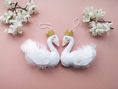 two white swans with gold crowns on their heads are sitting next to some flowers and branches