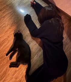 a woman laying on the floor next to a black cat