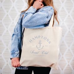 a woman holding a tote bag that says hampton's coastal club on it