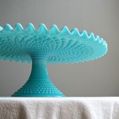 a blue glass dish sitting on top of a white tablecloth covered table next to a gray wall