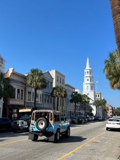 a blue jeep driving down a street next to tall buildings with a clock tower in the background