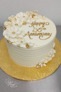 a white and gold wedding cake with flowers on the top is sitting on a golden plate