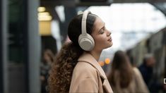 a woman with headphones on standing in front of a train at a subway station