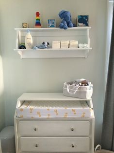 a baby's nursery room with white furniture and toys on shelves above the crib