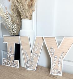 two wooden letters sitting on top of a table next to a vase with dried flowers