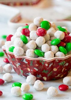 a red bowl filled with white and green candies on top of a table next to other candy