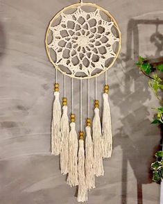 a white and beige dream catcher hanging on a wall next to a potted plant