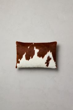 a brown and white cowhide pillow on a gray wall