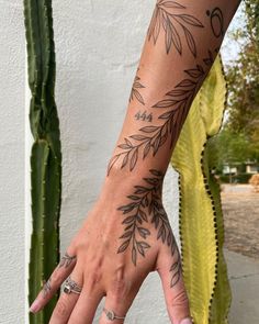 a woman's hand with tattoos on it and a cactus in the back ground