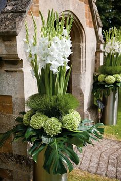 two metal vases with flowers and greenery in front of an old brick building