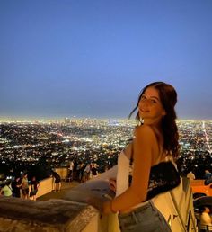 a woman standing on top of a tall building next to a cityscape at night