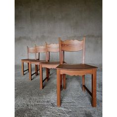 three wooden chairs sitting next to each other in front of a cement wall and concrete floor