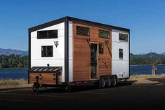 a tiny house on wheels parked in a parking lot next to a body of water