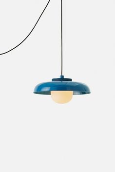 a blue pendant light hanging from a black cord on a white wall, with the ceiling in the background