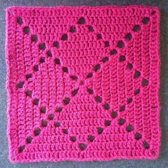 a pink crocheted square with hearts on it sitting on top of a gray surface