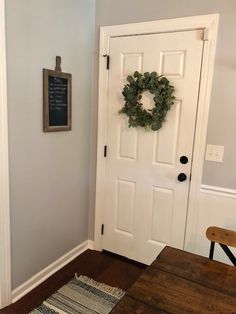 a door with a wreath hanging on the wall next to a wooden table and chair