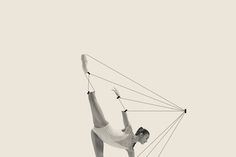 a man is doing aerial acrobatics on a rope with one hand and the other leg