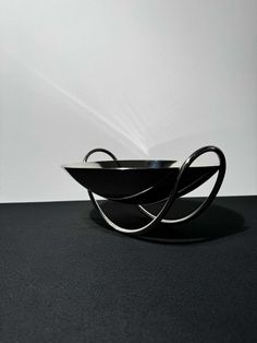 a black bowl sitting on top of a table next to a white wall in the background