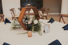 an arrangement of flowers and greenery on a white table cloth with blue napkins