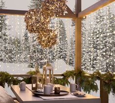 a dining room table set for christmas dinner with lights hanging from the ceiling and snow covered trees in the background