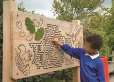 a young boy standing next to a wooden board with mazes and plants on it