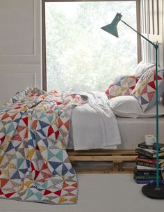 a bed sitting next to a window with a blanket and pillows on top of it