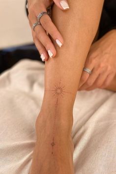 a woman with white nails and a star tattoo on her left leg, sitting on a bed