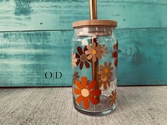 a glass jar with flowers painted on the side and a straw in the top is sitting on a table