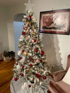 a white christmas tree with red and gold ornaments on it in a living room next to a chair