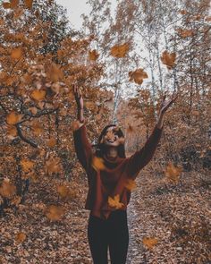 a woman is standing in the leaves with her hands up