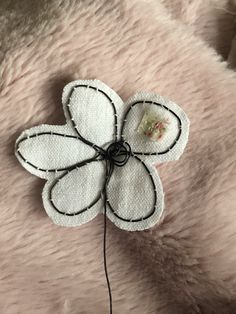 a close up of a flower on a pink fur surface with black string and thread