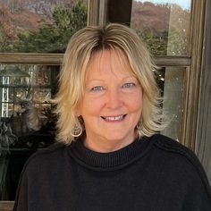 a woman with blonde hair smiling in front of a window