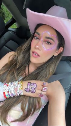 a woman with pink makeup wearing a cowboy hat and holding her hand up to her face