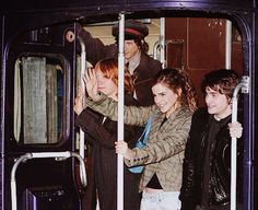 three people are standing on the door of a purple train and one person is holding their hands up