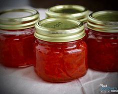 four jars filled with red liquid sitting on top of a white tablecloth covered table